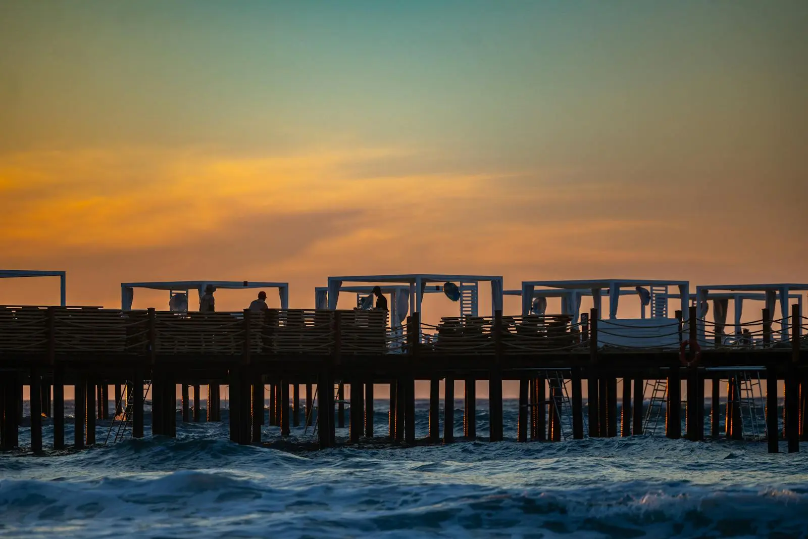 Photo by Besra Akar A tranquil sunset view of a pier in Kıbrıs with silhouetted figures.