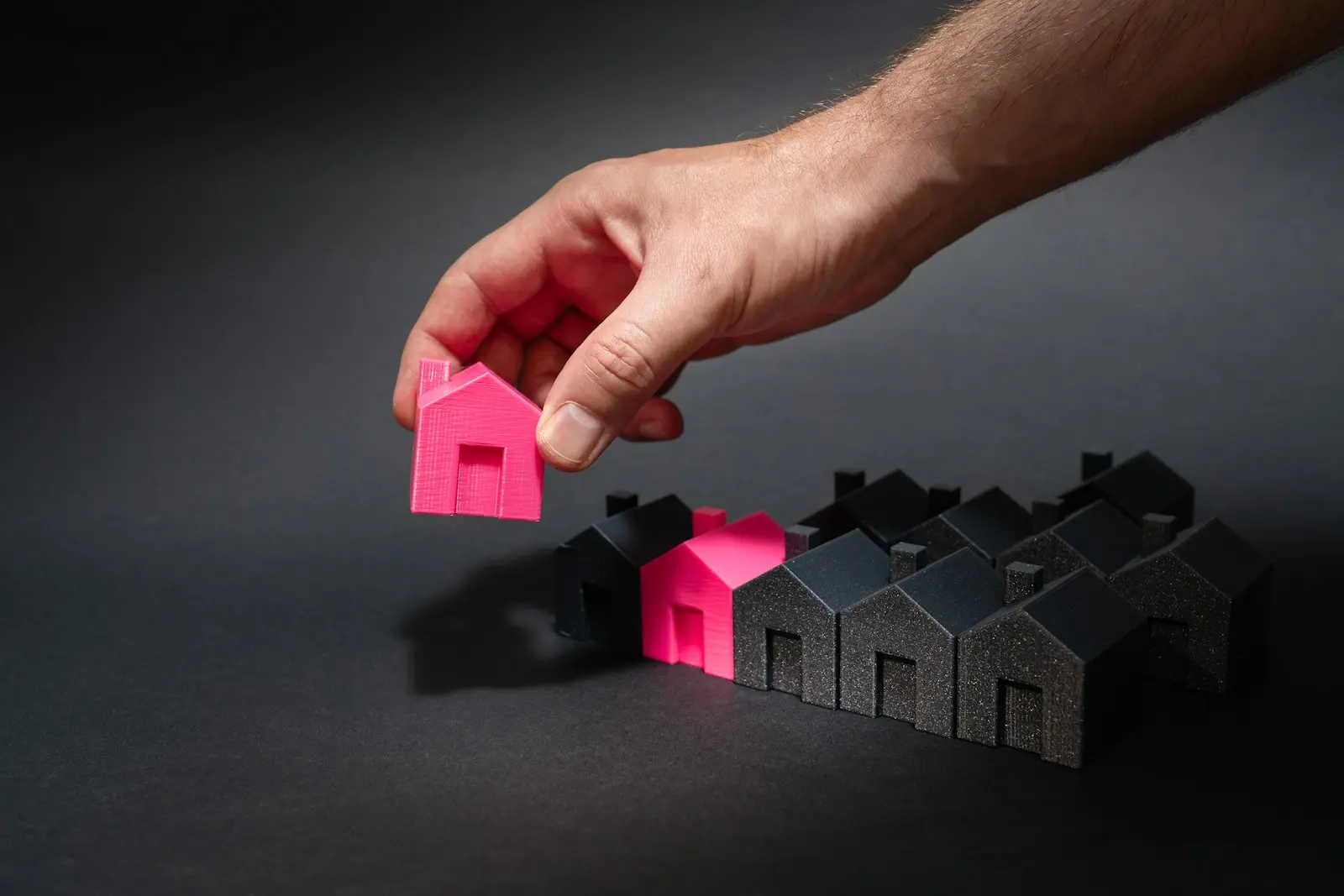 Photo by Jakub Żerdzicki A hand reaching for a pink house in front of a row of houses